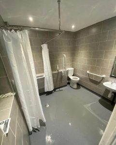 A disabled bathroom installation featuring non-slip flooring, grab bars, tiled walls and an accessible shower.