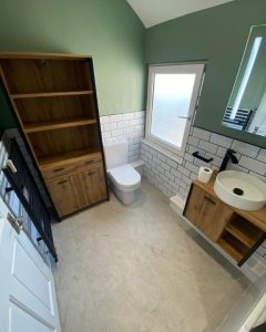 A new bathroom installation featuring a new toilet, sink with cabinet underneath, white tiled walls and a wooden cabinet.