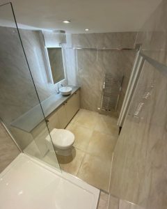 A new bathroom installation featuring tiled walls and floors, a long cabinet with a new sink and a WC.