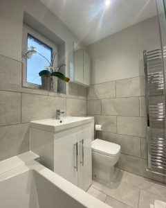 A new bathroom installation featuring a new sink and WC and grey tiled walls.