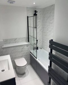 A new modern bathroom installation featuring grey tiled floors and walls, WC and shower over bath.