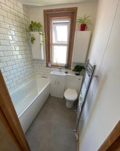 A new bathroom installation featuring a new bath, toilet, sink with cabinets and white tiled walls.