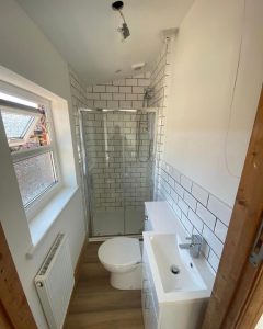A new bathroom installation featuring white tiled walls, a toilet and sink and a walk-in shower.