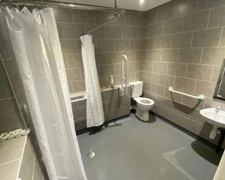A disabled bathroom installation featuring non-slip flooring, grab bars, tiled walls and an accessible shower.