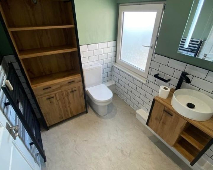 A new bathroom installation featuring a new toilet, sink with cabinet underneath, white tiled walls and a wooden cabinet.