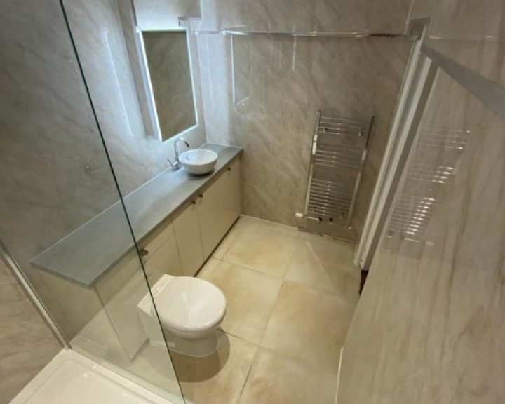 A new bathroom installation featuring tiled walls and floors, a long cabinet with a new sink and a WC.