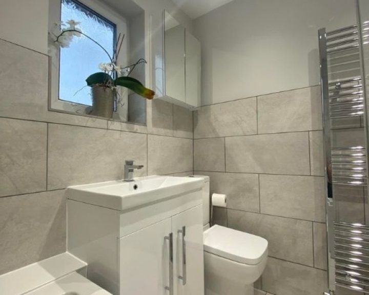 A new bathroom installation featuring a new sink and WC and grey tiled walls.