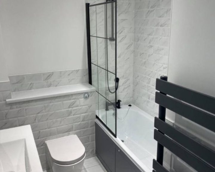 A new modern bathroom installation featuring grey tiled floors and walls, WC and shower over bath.
