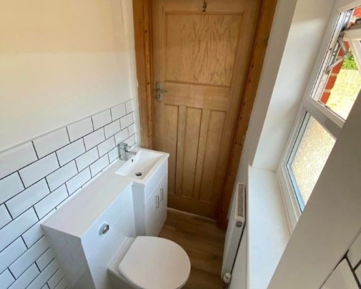 A new bathroom installation featuring white tiled walls, a toilet and sink and a new wooden door.