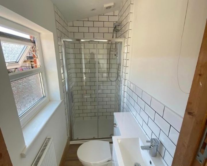 A new bathroom installation featuring white tiled walls, a toilet and sink and a walk-in shower.