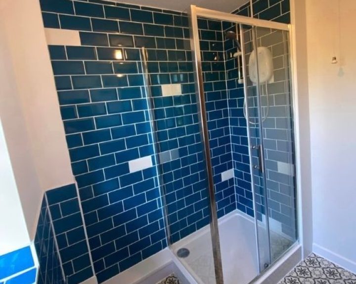 A new bathroom installation featuring blue tiled walls, a walk-in shower enclosure and vinyl flooring.