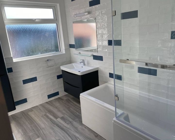 A new Basingstoke bathroom installation featuring blue and white tiled walls, a shower over bath, a new sink and vinyl flooring.