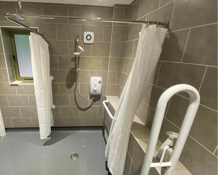 Disabled bathroom that has been installed including non-slip flooring, grey wall tiles and grab bars and rails installed on the walls.