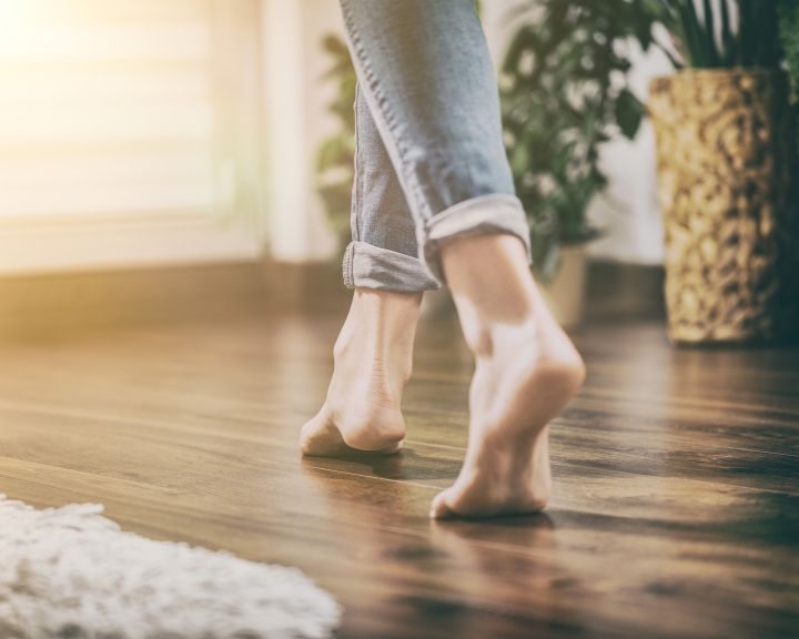 A woman walking barefoot on a wooden flooring that has underfloor heating installed underneath.